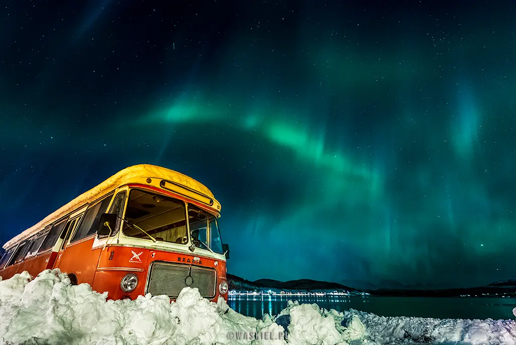 Obraz przedstawiający ciekawe ujęcie zorzy polarnej nad opuszczonym autobusem.